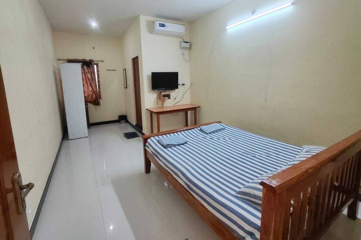A small, clean room with a single bed, a desk, a television, and an air conditioning unit.