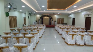 A spacious hall with rows of chairs, ceiling fans, and a stage with floral decorations. - Nalli Plaza (Omalur)