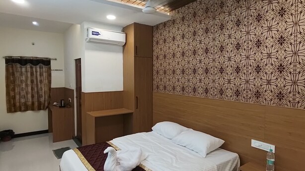 A modern hotel room with a large bed, a ceiling fan, an air conditioning unit, and a patterned wall. - Nalli Plaza (Omalur)
