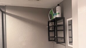 A bathroom with a toilet, a shelf with toiletries, and a shower area.