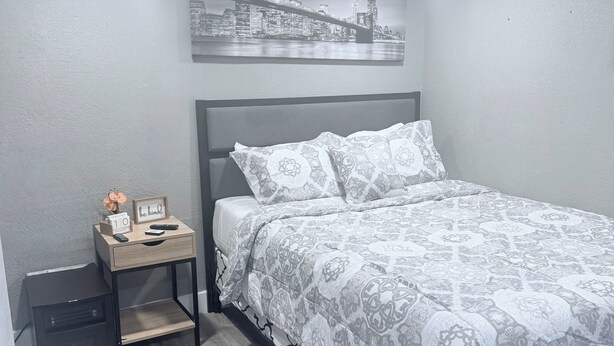 A bedroom with a bed, a nightstand, a wall-mounted picture, and a wooden floor.