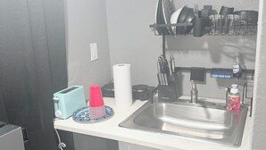 A compact kitchen with a sink, a dish rack, a toaster, and a trash can.