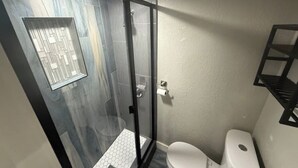 A small bathroom with a glass shower enclosure, a toilet, and a white sink.