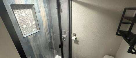 Een kleine badkamer met een douchecabine van glas, een toilet en een witte wastafel.