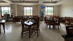 A spacious dining area with multiple tables and chairs, ceiling fans, and large windows providing natural light. - KRISHNA ANANDAM PALACE (Mathura)