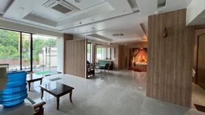 A spacious lobby with a modern design, featuring a seating area with tables and chairs, a large water dispenser, and a decorative wall with a fire feature. - KRISHNA ANANDAM PALACE (Mathura)