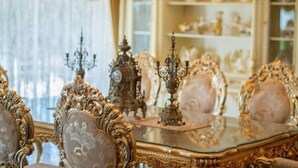 Una habitación ornamentada con una mesa de vidrio, sillas ornamentales y un candelabro.
