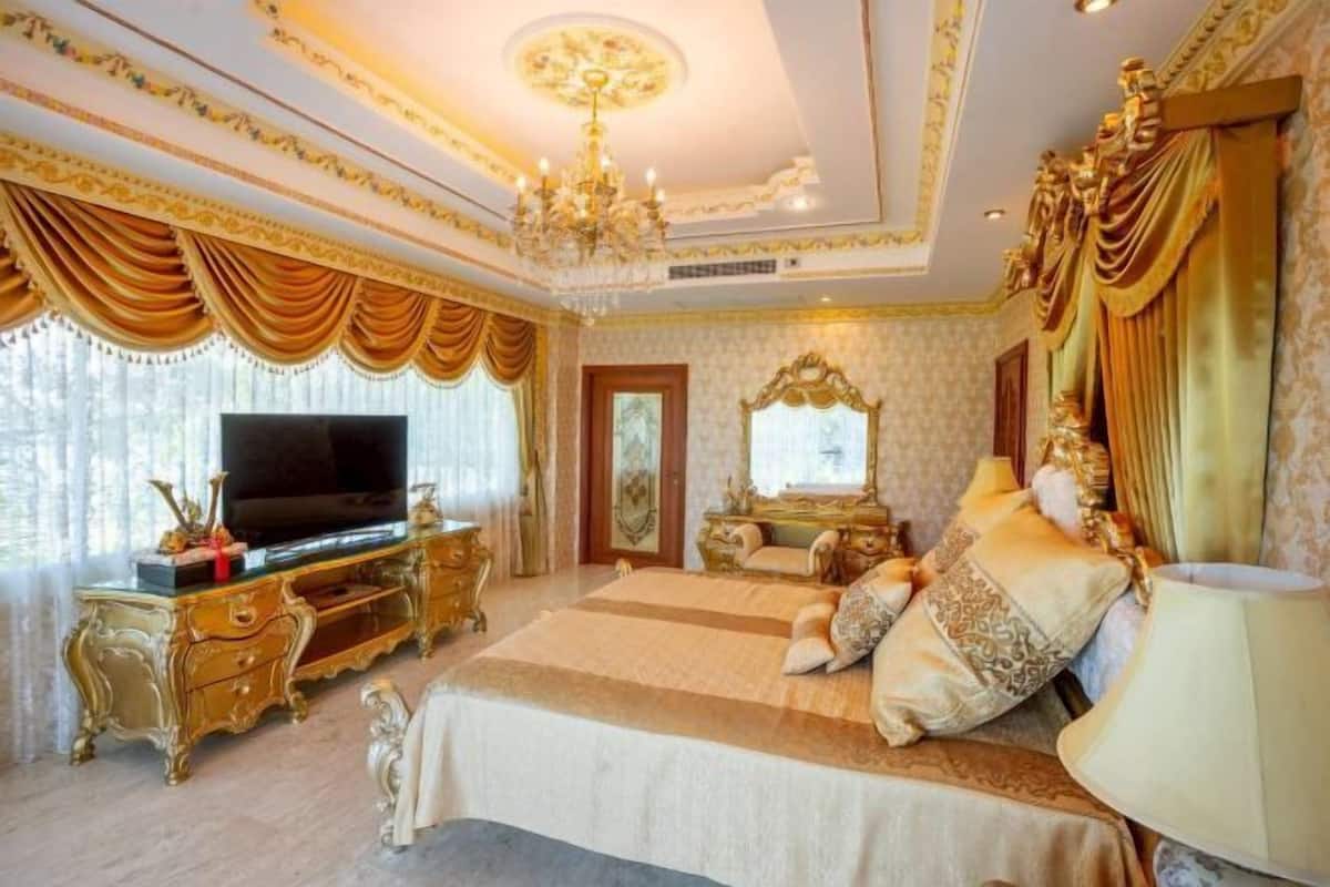 A luxurious bedroom with a large bed, a television, ornate furniture, and a chandelier.