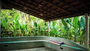 A concrete swimming pool with a curved edge, surrounded by lush green tropical plants. - Virama Gokarna (Gokarna)