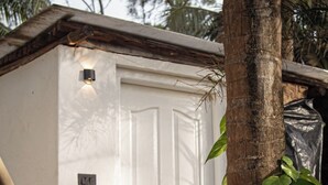 A white door with a small light above it, a wooden doorbell, and a plant growing beside the door. - Virama Gokarna (Gokarna)