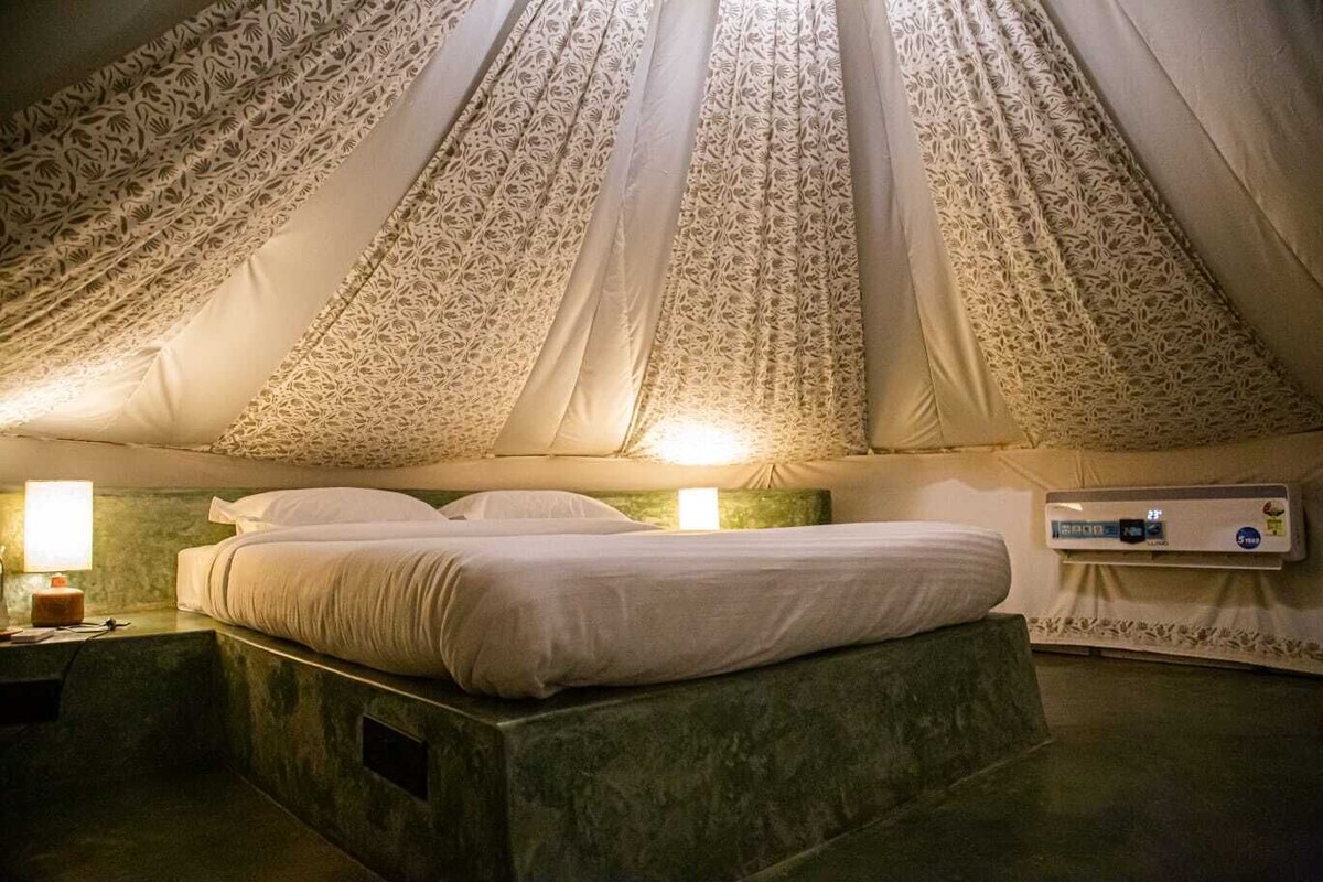 Habitación tipo tienda de campaña con una cama, dos lámparas de noche y un termostato en la pared.