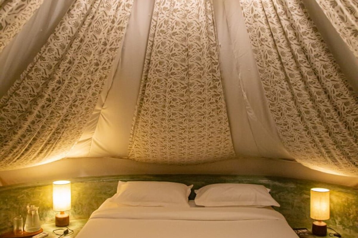 Una habitación tipo tienda de campaña con cama, cortinas estampadas y dos lámparas de noche.