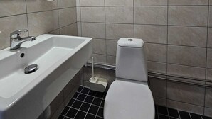 A bathroom with a white sink, a toilet, and a hand soap dispenser on the wall. - Nox Hotel (Huddinge)