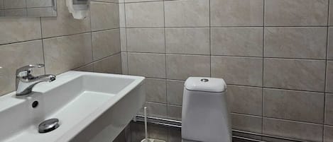 A bathroom with a white sink, a toilet, and a hand soap dispenser on the wall.