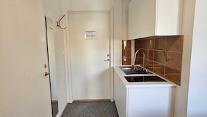 A narrow hallway leading to a kitchen with white cabinets, a sink, and a tiled backsplash. - Nox Hotel (Huddinge)