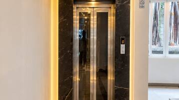 Un ascensor moderno con pantalla digital, suelo de mármol y puerta de vidrio.