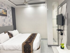 A modern hotel room with a large bed, a flat-screen TV mounted on the wall, and a small potted plant on a white console table.