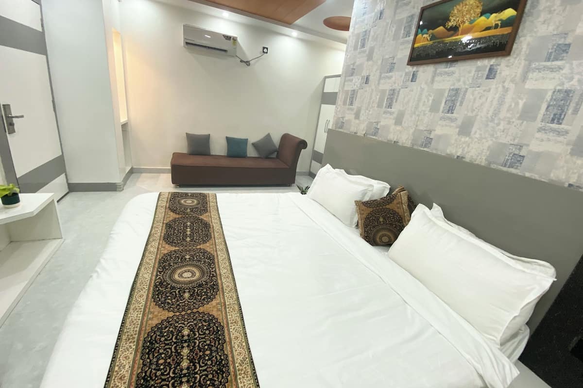 A neatly arranged bedroom with a large bed, a sofa, a wall-mounted air conditioner, and a framed picture on the wall.