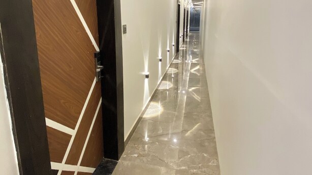A modern hotel corridor with a polished marble floor, a wooden door with a geometric design, and a sign indicating room number 101. - Hotel Manor Ganges (Varanasi)