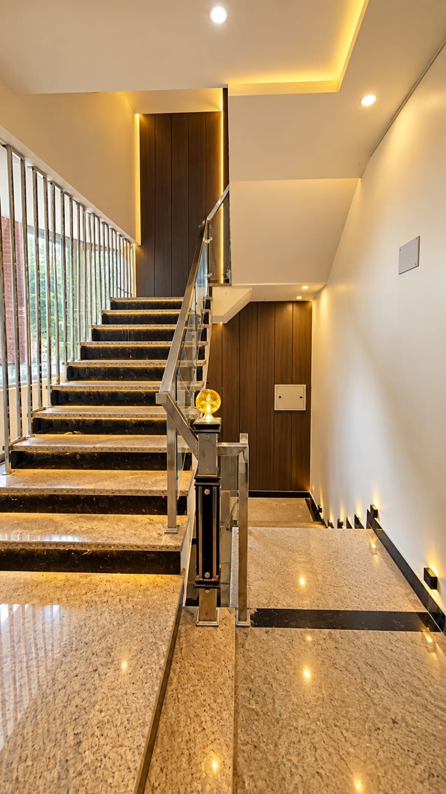 Un interior moderno con una escalera, suelo de piedra pulida y barandilla de vidrio.