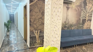 A modern lobby with a marble floor, a blue sofa, a decorative wall with a nature mural, and a potted plant. - Hotel Manor Ganges (Varanasi)