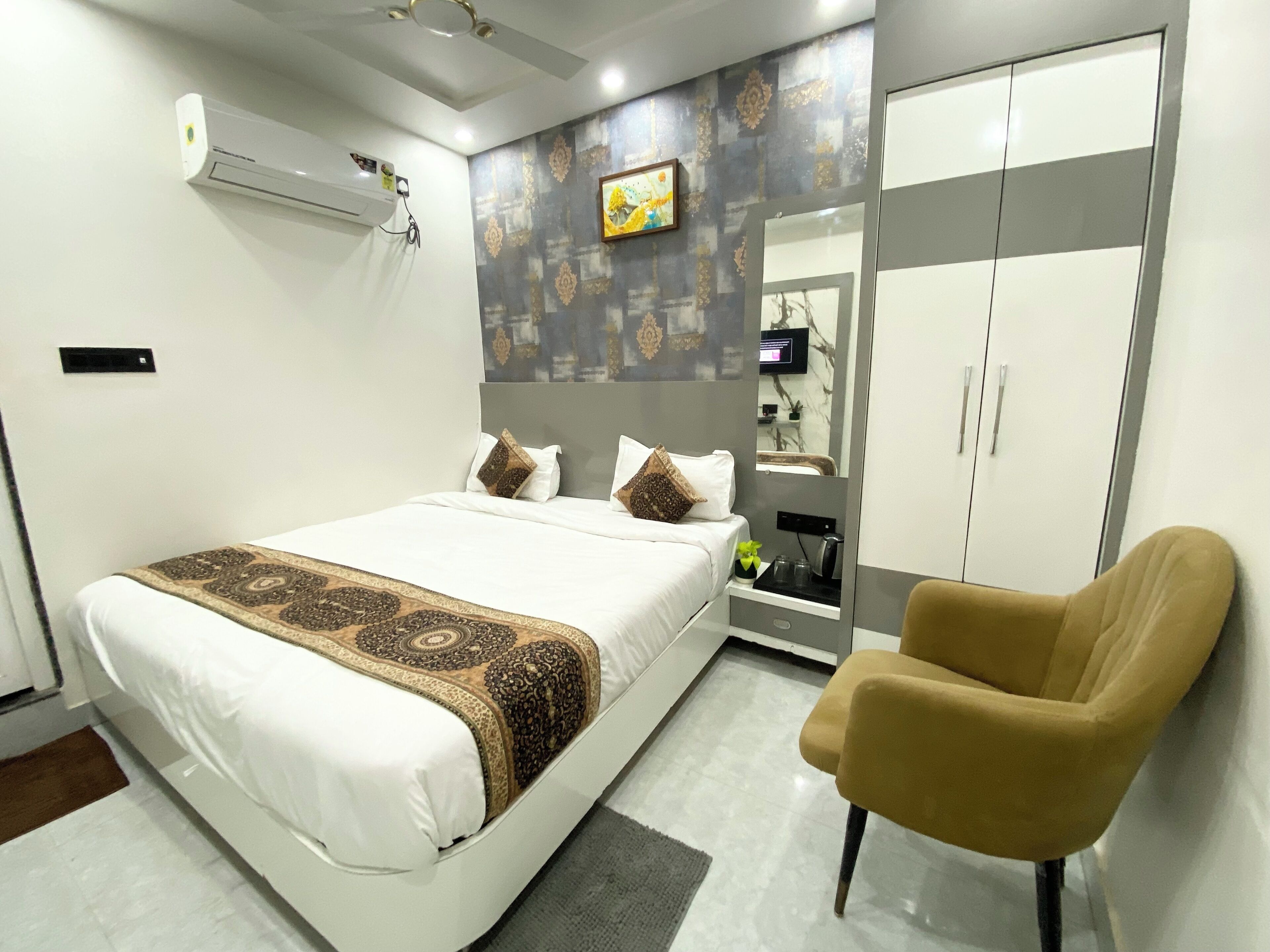 Un dormitorio moderno con cama, una silla, un armario y un televisor en la pared.