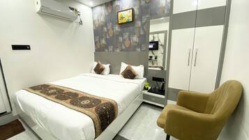 Un dormitorio moderno con cama, una silla, un armario y un televisor en la pared.