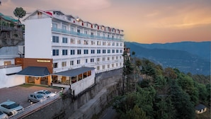 A multi-story hotel with a prominent entrance, a covered outdoor area, and a view of the surrounding landscape. - The Grand Welcome Hotel  (Shimla)