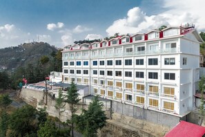 Een hotel met meerdere verdiepingen, een witte gevel en balkons. Het hotel ligt op een heuvel met uitzicht op een heuvel in de verte.
