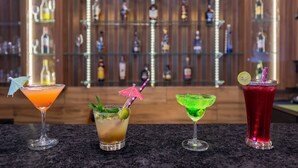 Four cocktails on a bar counter with a background of shelves stocked with bottles. - The Grand Welcome Hotel  (Shimla)