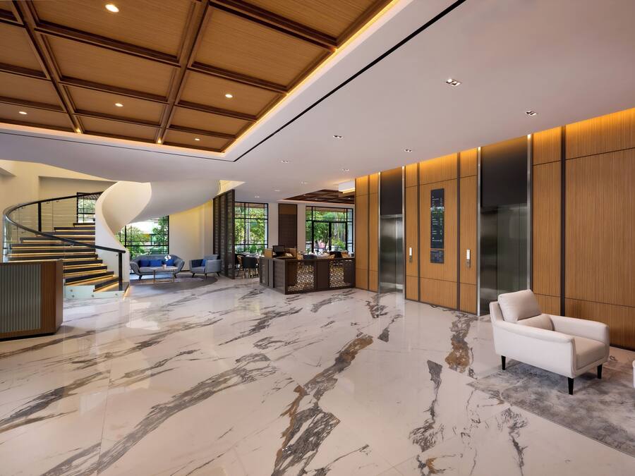 A modern lobby with a marble floor, a curved staircase, and a reception desk.