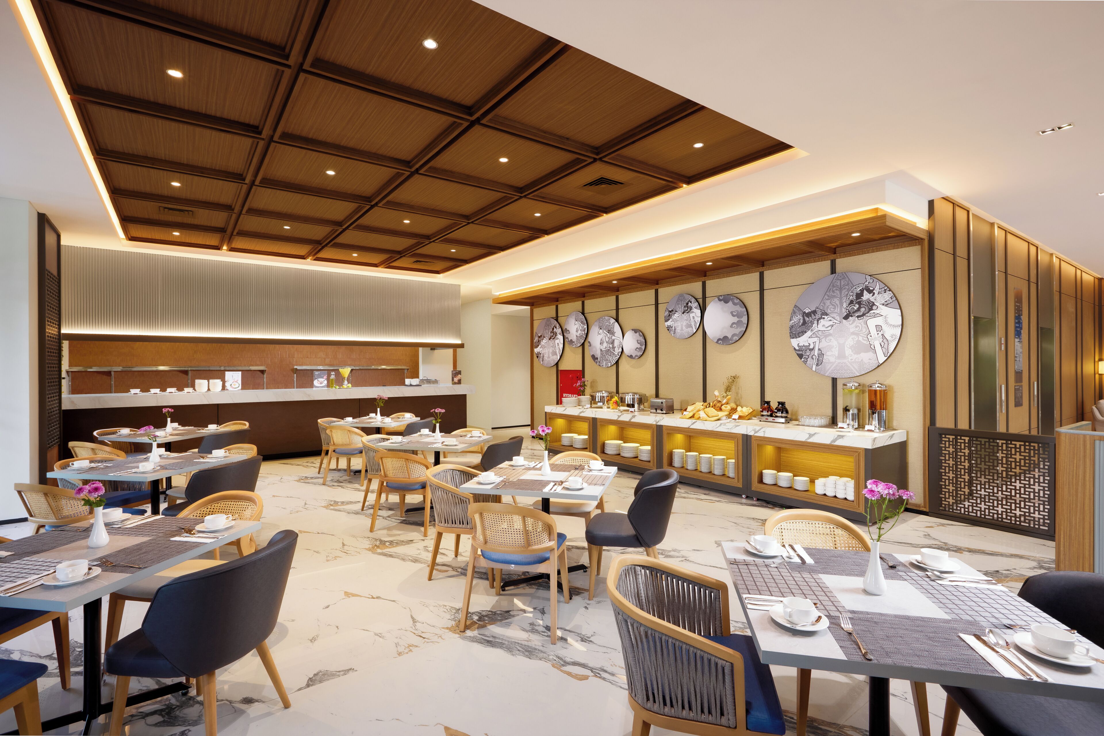 Uma sala de jantar de hotel com várias mesas e cadeiras, um balcão de buffet e um teto com iluminação embutida.
