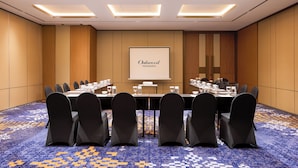 A conference room with a long table, chairs, a projector screen, and a carpeted floor. - Oakwood Yogyakarta (Yogyakarta)