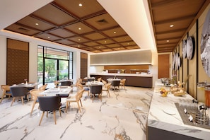 A modern dining area with marble flooring, wooden ceiling panels, and a buffet setup. - Oakwood Yogyakarta (Yogyakarta)
