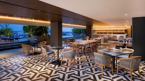 A restaurant with a geometric patterned floor, wooden furniture, and a view of the cityscape. - Oakwood Yogyakarta (Yogyakarta)