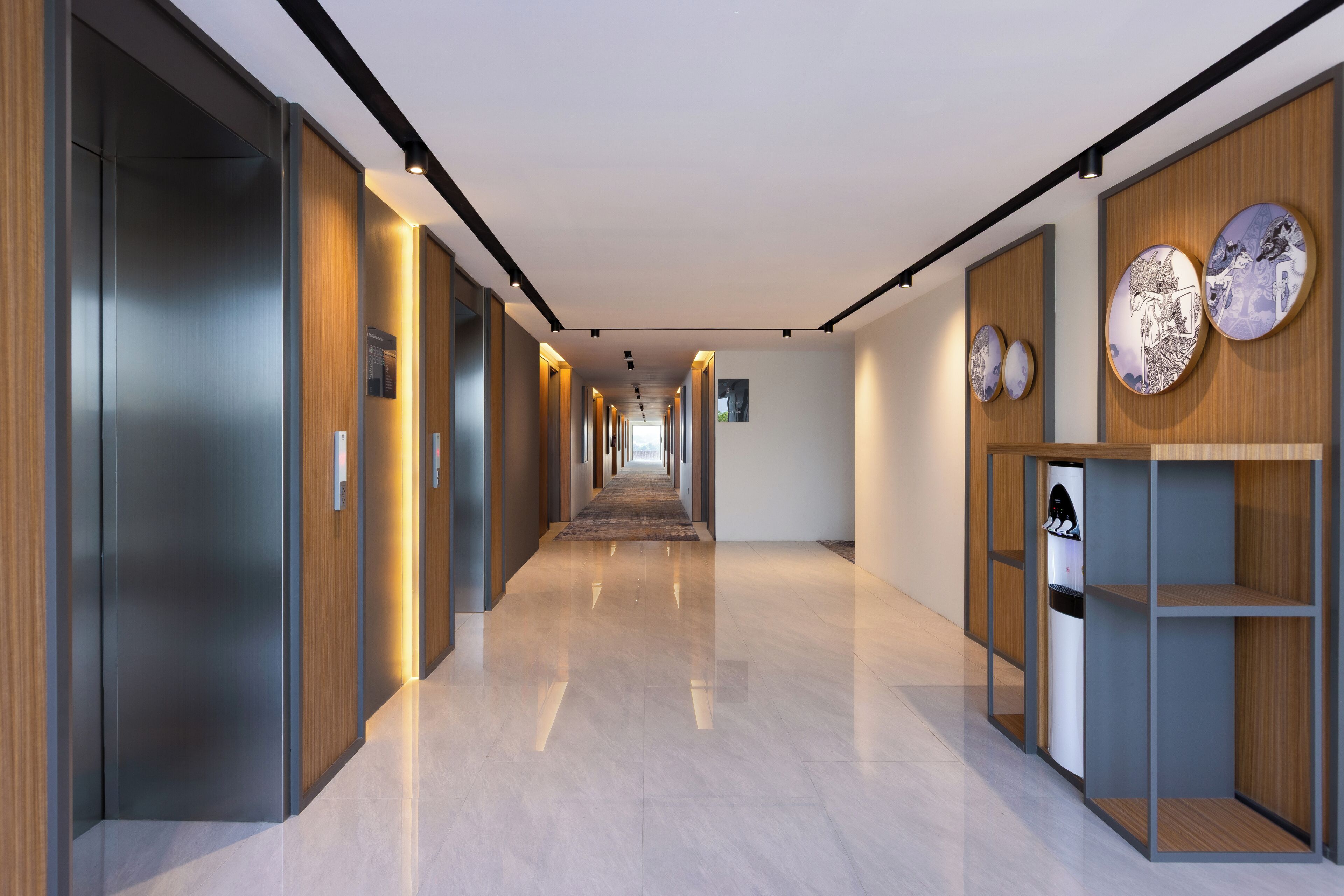 A modern hallway with a long corridor, wooden paneling on the walls, and a water dispenser on the right.