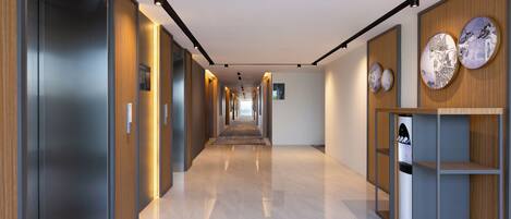 A modern hallway with a long corridor, wooden paneling on the walls, and a water dispenser on the right.