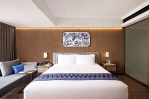 Une chambre d’hôtel moderne dotée d’un grand lit, d’un bureau avec un ordinateur portable, d’une table de chevet avec une lampe et d’une œuvre d’art accrochée au mur.