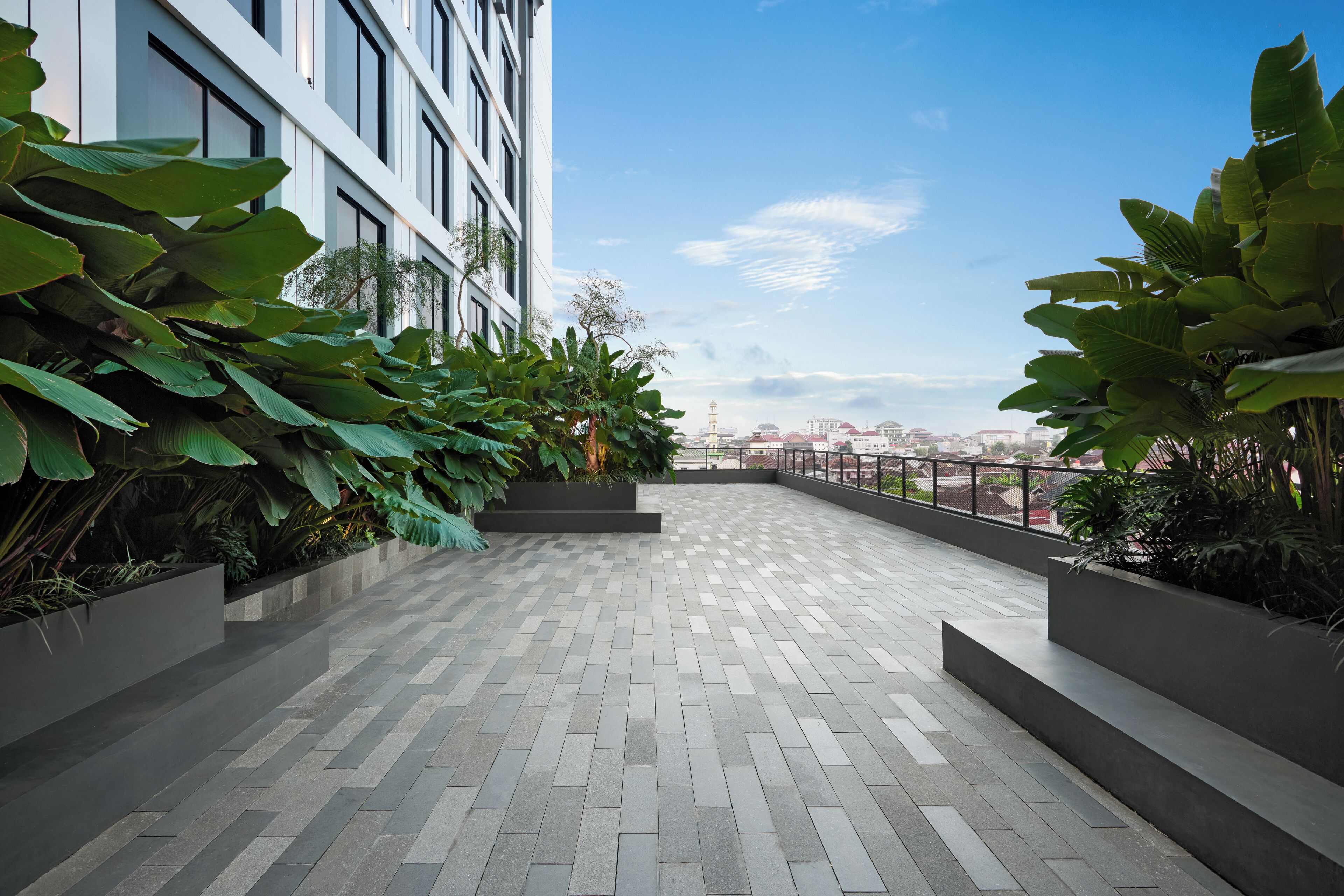 A rooftop terrace with a view of the city skyline, featuring a modern building with large windows and a paved walkway.