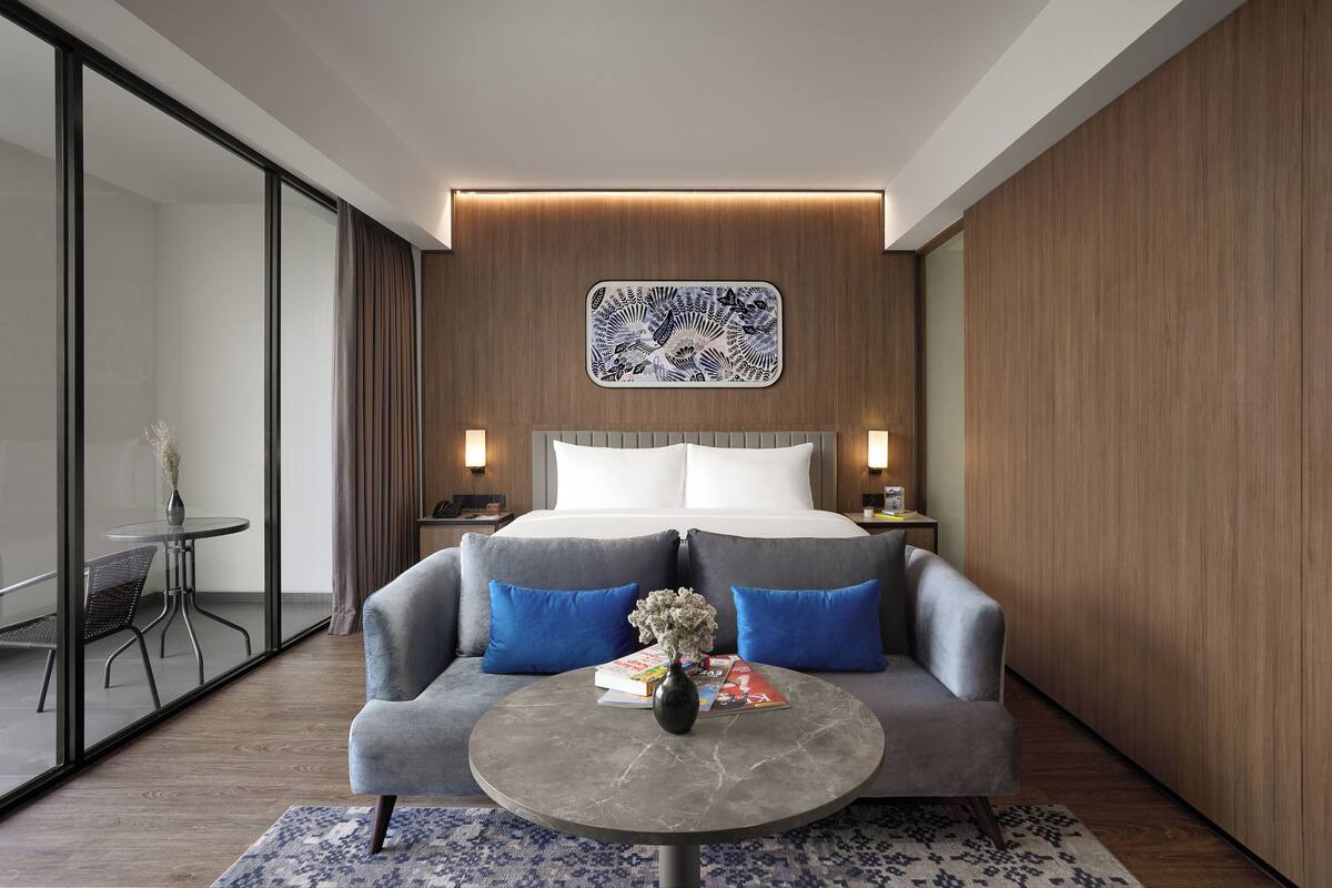 A modern hotel room with a large bed, a sofa, a coffee table, and a decorative wall piece.
