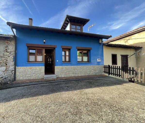 Ein zweistöckiges Gebäude mit blauer Fassade, Steinuntergrund und Holzzaun.