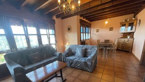 A cozy living area with a sofa, a wooden coffee table, and a dining table with chairs. There is a kitchen area with cabinets and a clock on the wall. - Casa Carmen for 8-9 people in Biedes (Biedes)