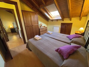 Ein Schlafzimmer mit zwei Betten, einem Holzschrank, einem Oberlicht und einem kleinen Nachttisch mit Lampe.