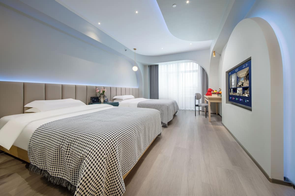 A modern hotel room with two beds, a desk, and a large window.