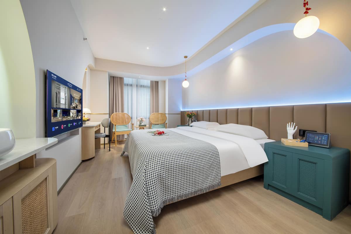 A modern hotel room with a large bed, a desk, a chair, and a television.