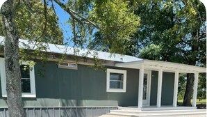 Une maison de plain-pied avec un porche couvert, une cour clôturée et un arbre à l’avant.