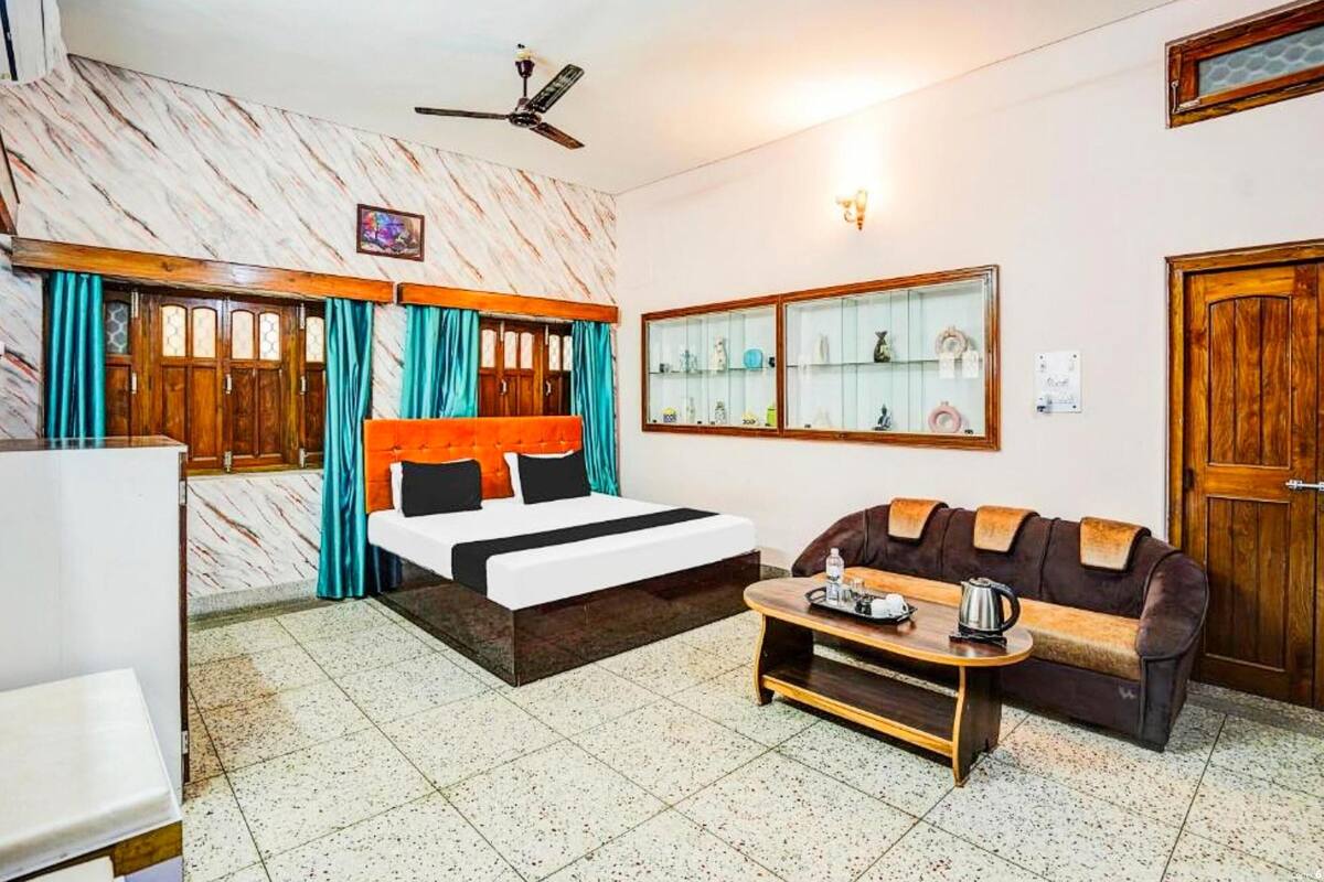Une chambre d’hôtel comprenant un lit, un canapé, une table basse, un ventilateur de plafond et une étagère murale agrémentée d’objets décoratifs.