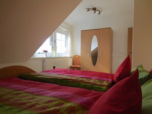 Un dormitorio con techo inclinado, una cama con ropa de cama floral, un armario de madera, una silla y una ventana con vistas.