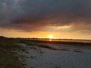 Un coucher de soleil sur un paysage plat, avec une étendue d’eau et un horizon lointain.