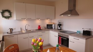 Een moderne keuken met witte kasten, een roestvrijstalen spoelbak, een magnetron, een koffiezetapparaat en een broodrooster. Op de tafel staat een vaas met tulpen.